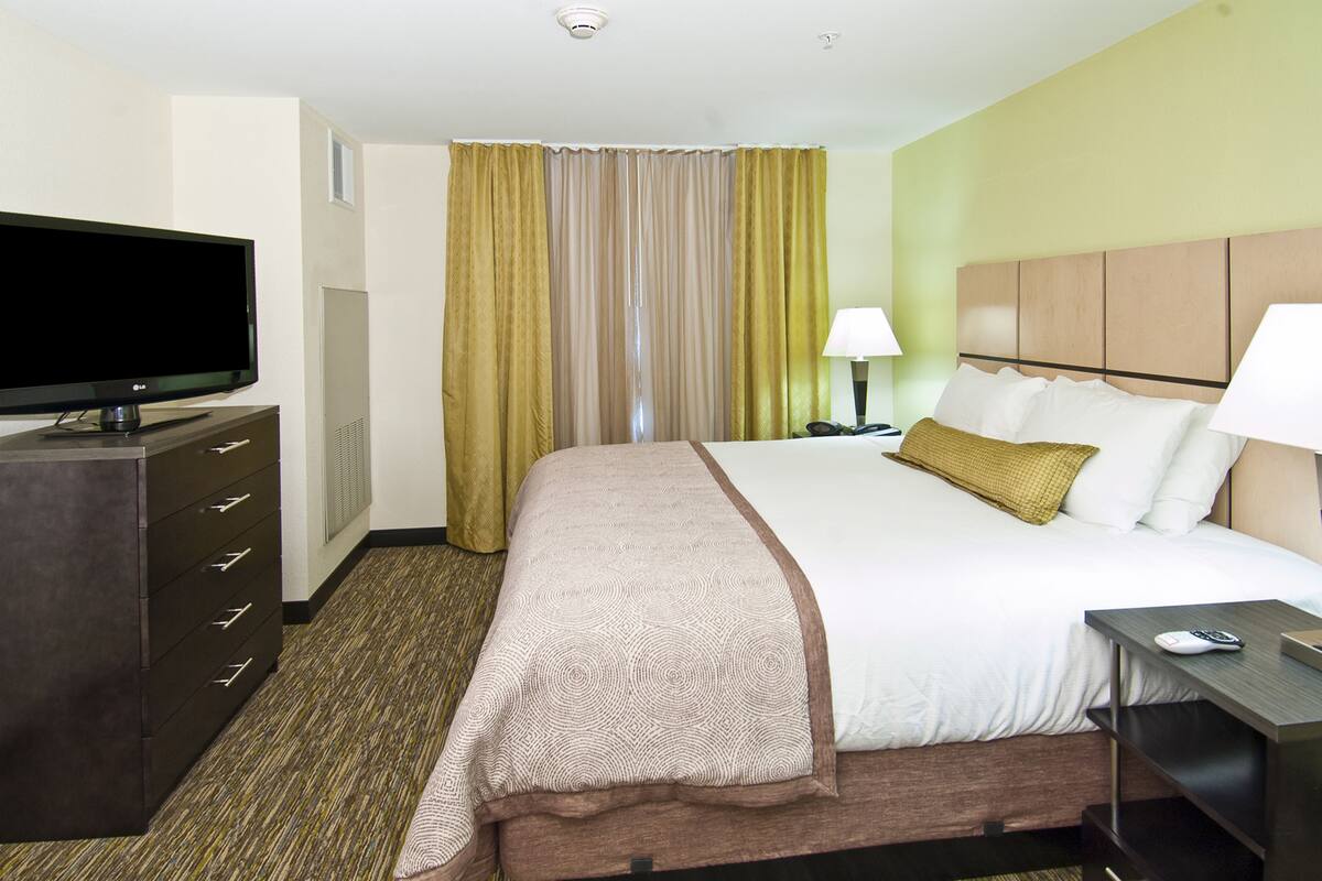 A hotel room with a bed, a TV on a dresser, a lamp, and a bedside table.