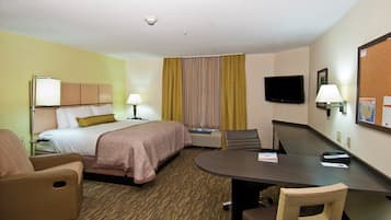 Una habitación de hotel con cama, escritorio, silla, televisión y un tablón de anuncios.