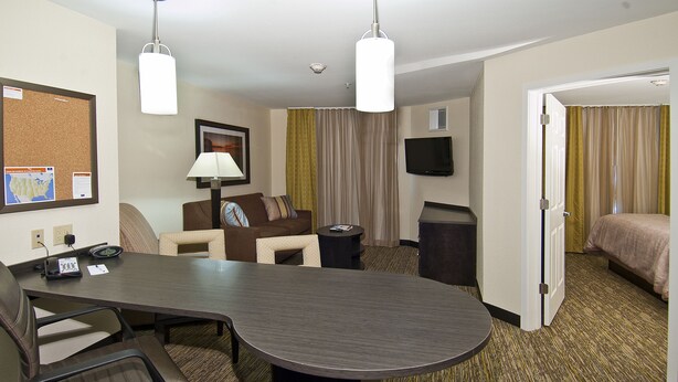 A hotel room with a conference table, chairs, a bed, a TV, and a door leading to another room.