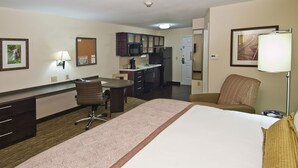 A hotel room with a bed, a desk, a chair, a kitchenette, and a bathroom.