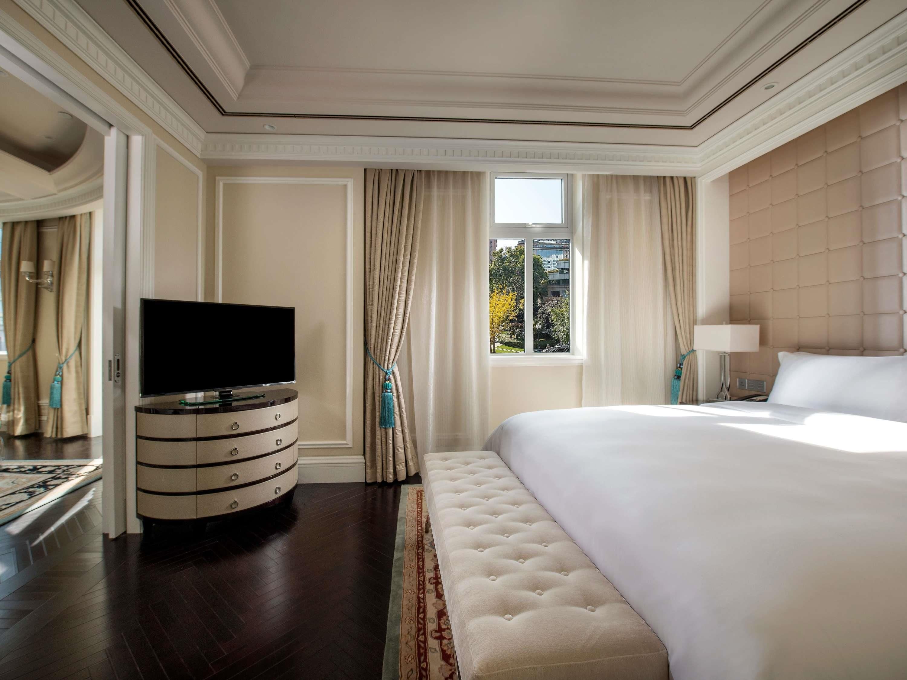 A hotel room with a large bed, a TV on a side table, and a window with curtains.