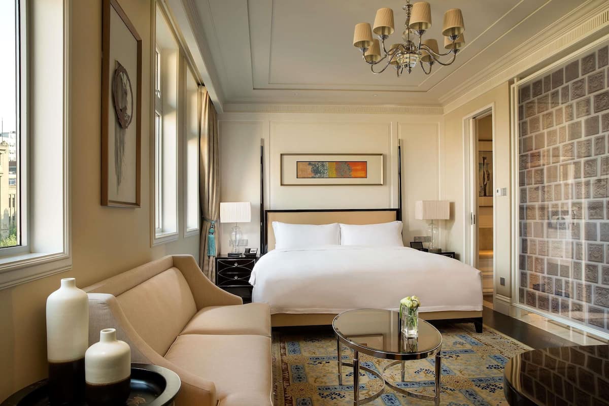 A hotel room with a bed, a sofa, a small table, a chandelier, and a decorative wall.