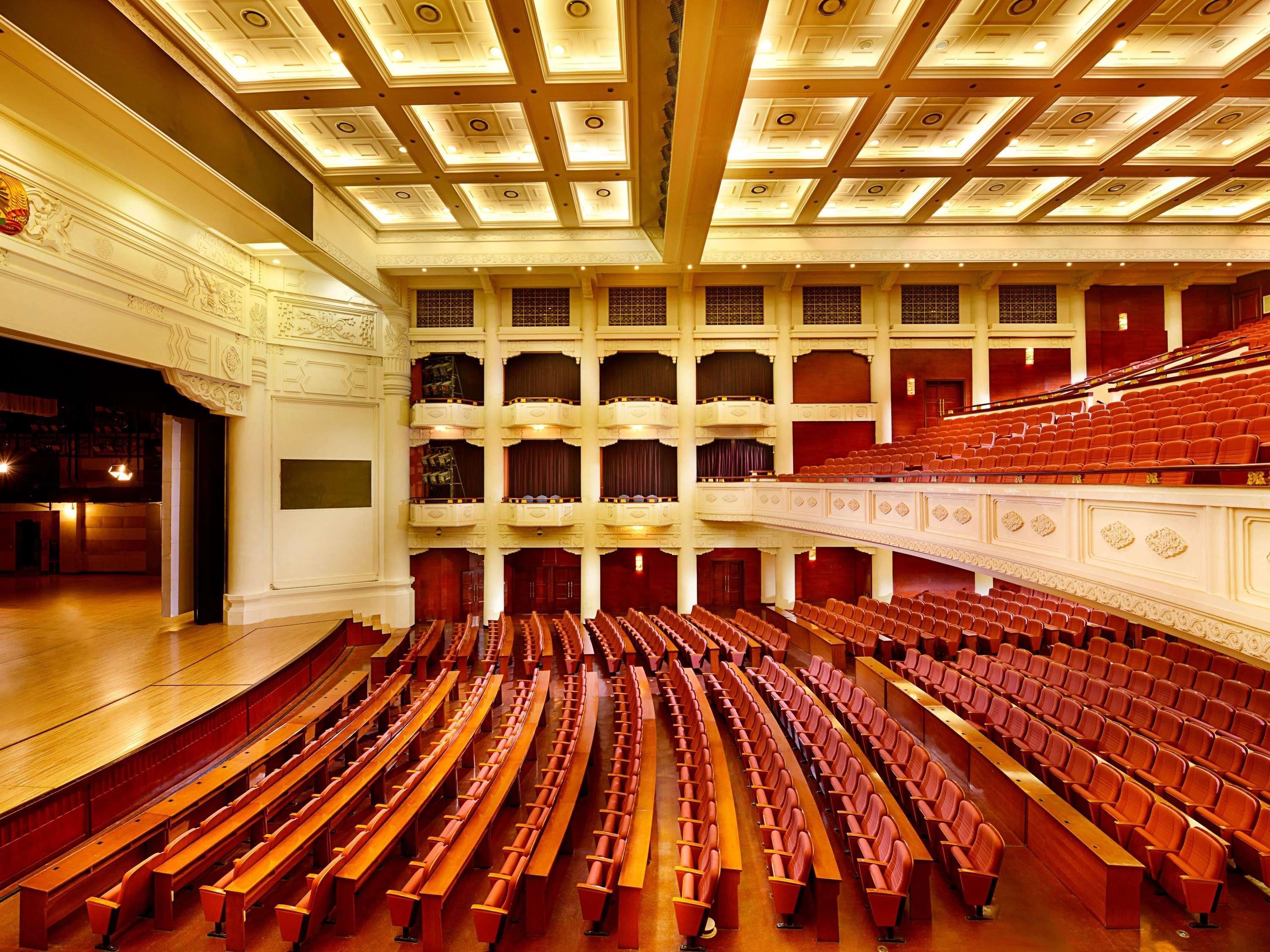 A large auditorium with tiered seating, ornate ceiling, and a stage area.