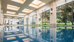 A large indoor swimming pool with clear glass walls, a tiled floor, and a ceiling with skylights.