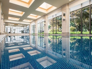 Une grande piscine intĂ©rieure aux parois en verre transparent, dotĂ©e dâun sol carrelĂ© et dâun plafond agrĂ©mentĂ© de lucarnes.