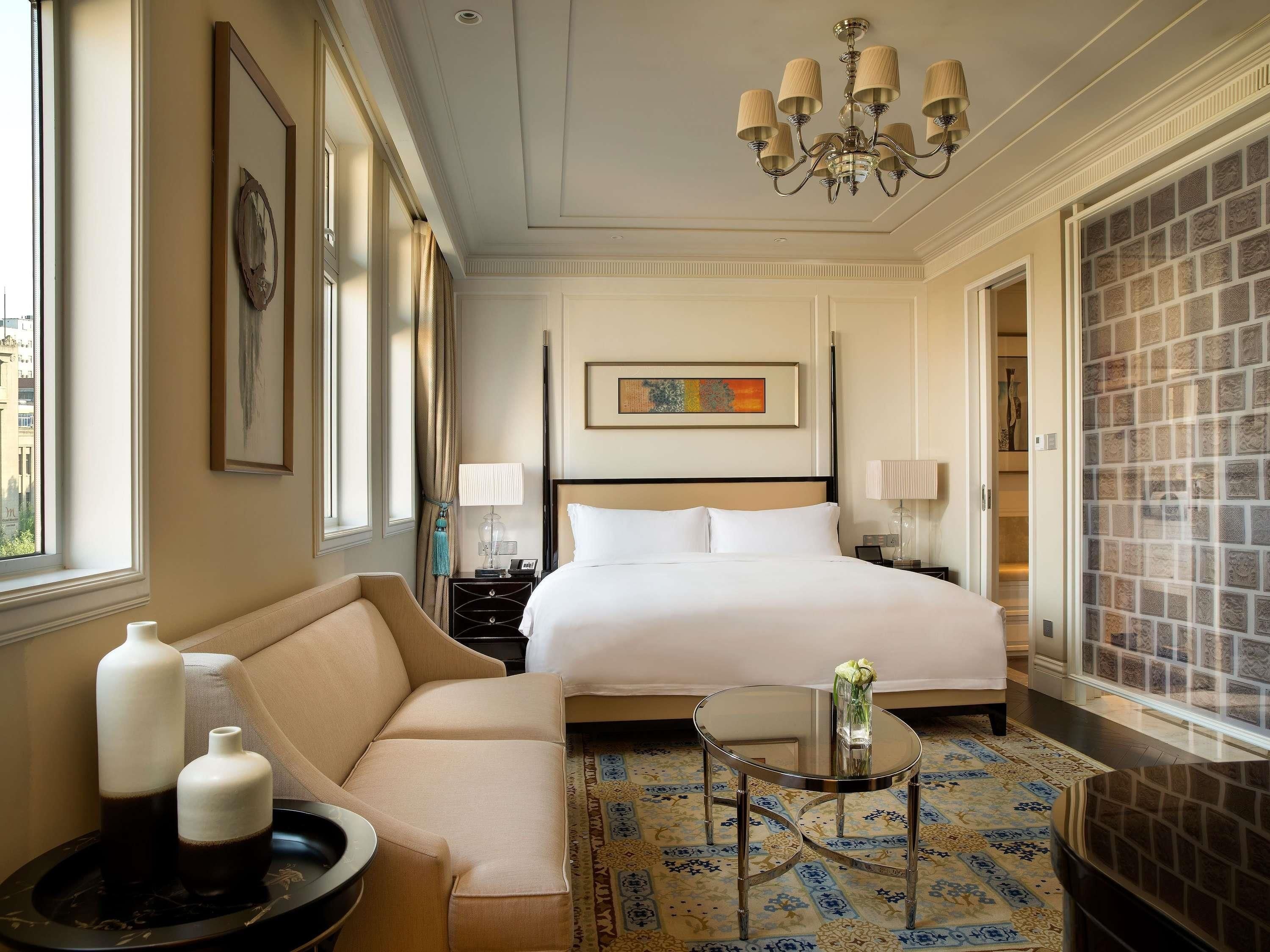 A hotel room with a bed, a sofa, a small table, a chandelier, and a decorative wall.