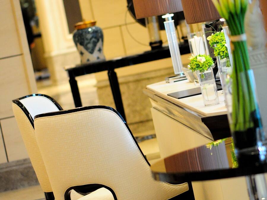 A dining area with a table set for two, featuring a vase with green flowers, a lamp, and a decorative plate.
