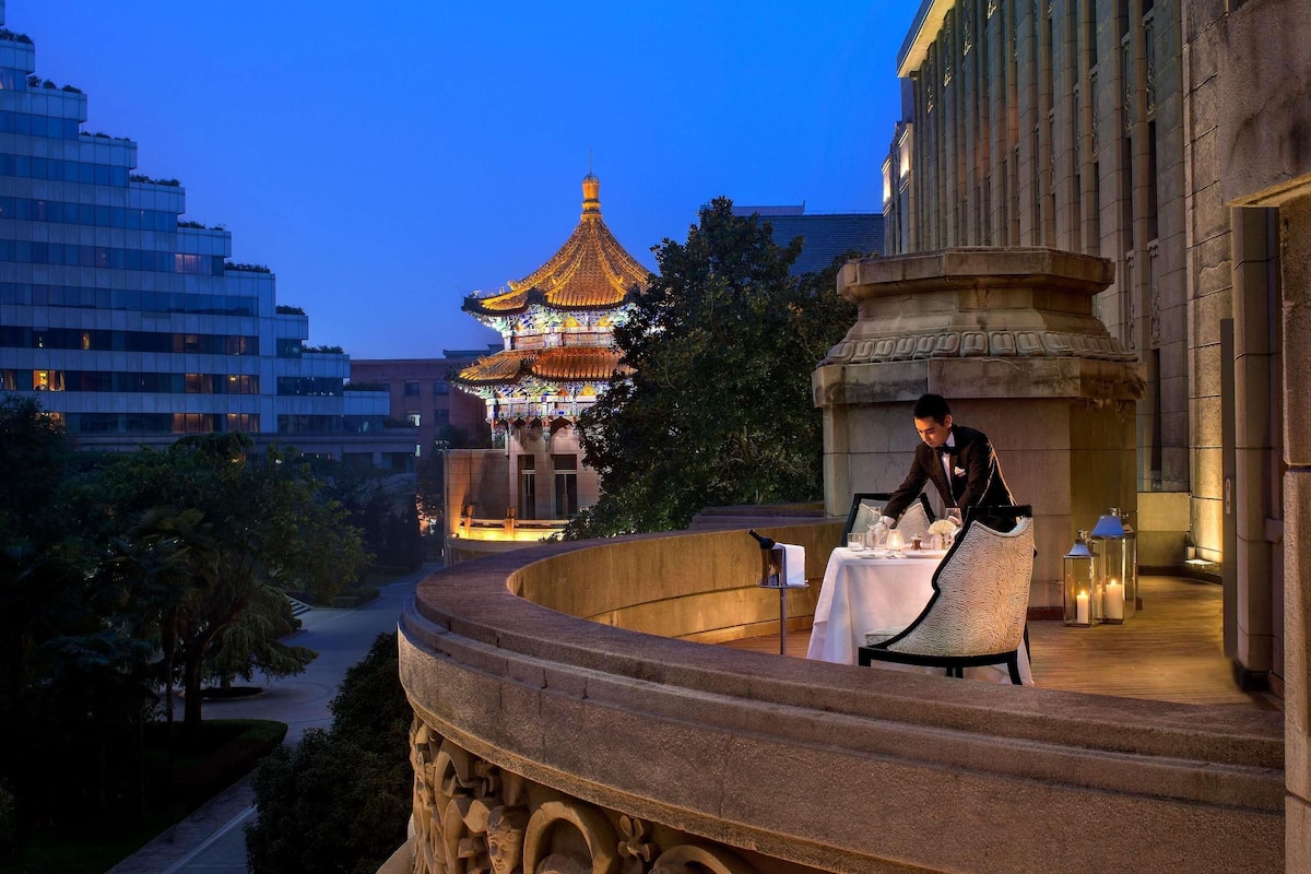A dining area with a table set for two, a waiter, and a traditional building in the background.