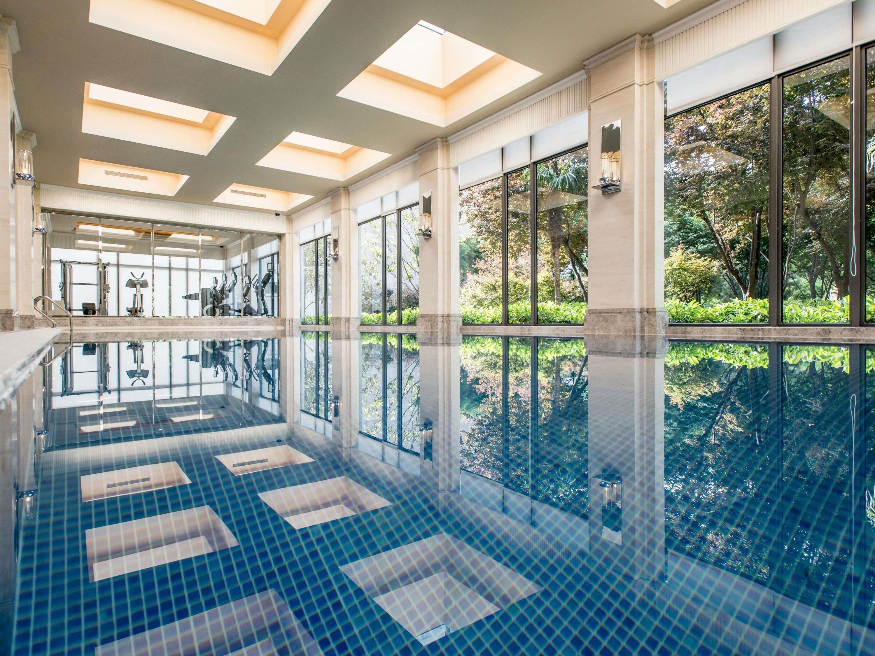 Una amplia piscina interior con paredes de vidrio transparente, suelo de baldosas y techo con tragaluces.