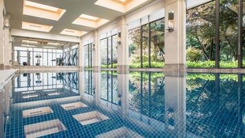Una amplia piscina interior con paredes de vidrio transparente, suelo de baldosas y techo con tragaluces.