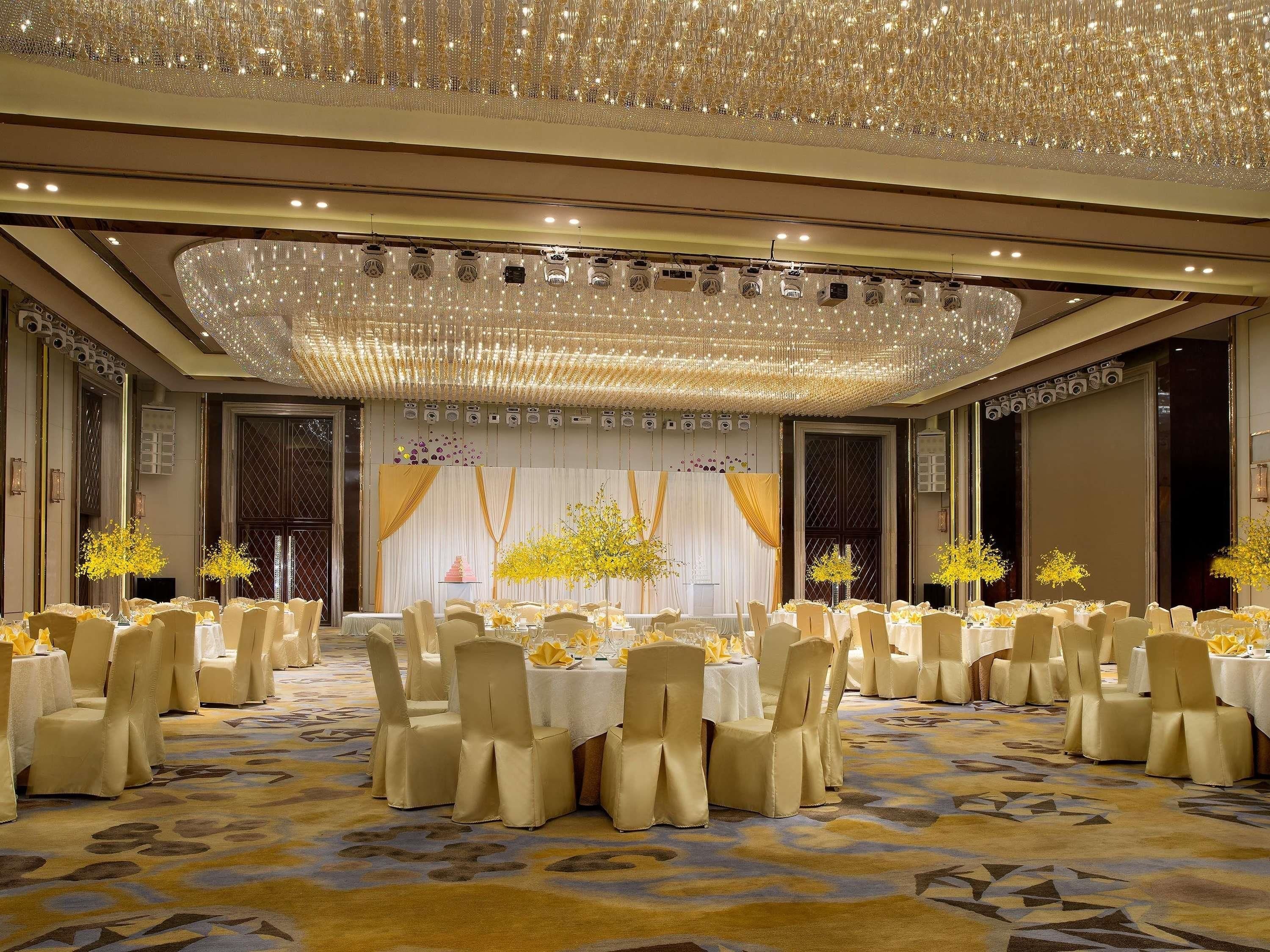 Un salón de banquetes con mesas redondas, sillas y un escenario con cortinas.