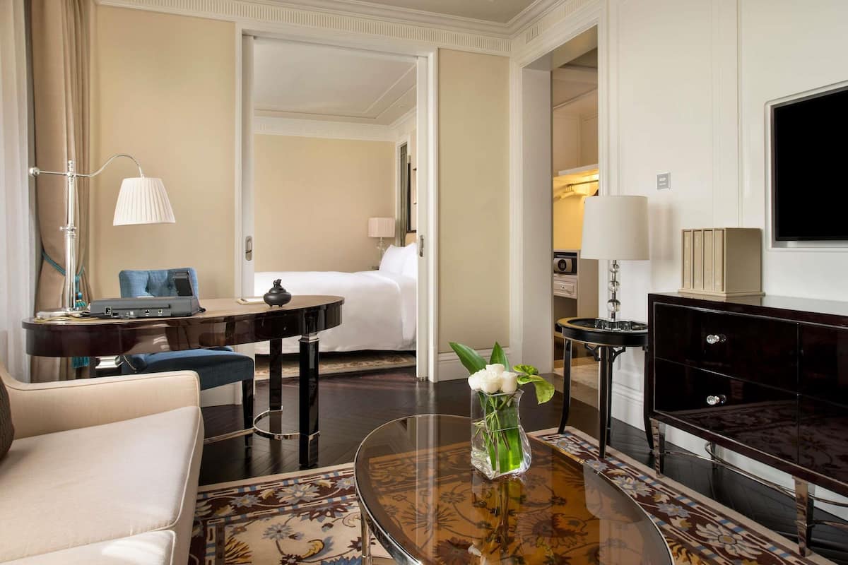 A hotel room with a bed, a desk with a lamp, a coffee table with a vase, and a TV on the wall.