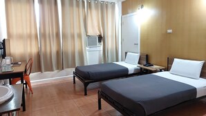 A hotel room with two beds, a desk with a chair, a small table, and a wall-mounted air conditioning unit. - My Hotel (Davao)