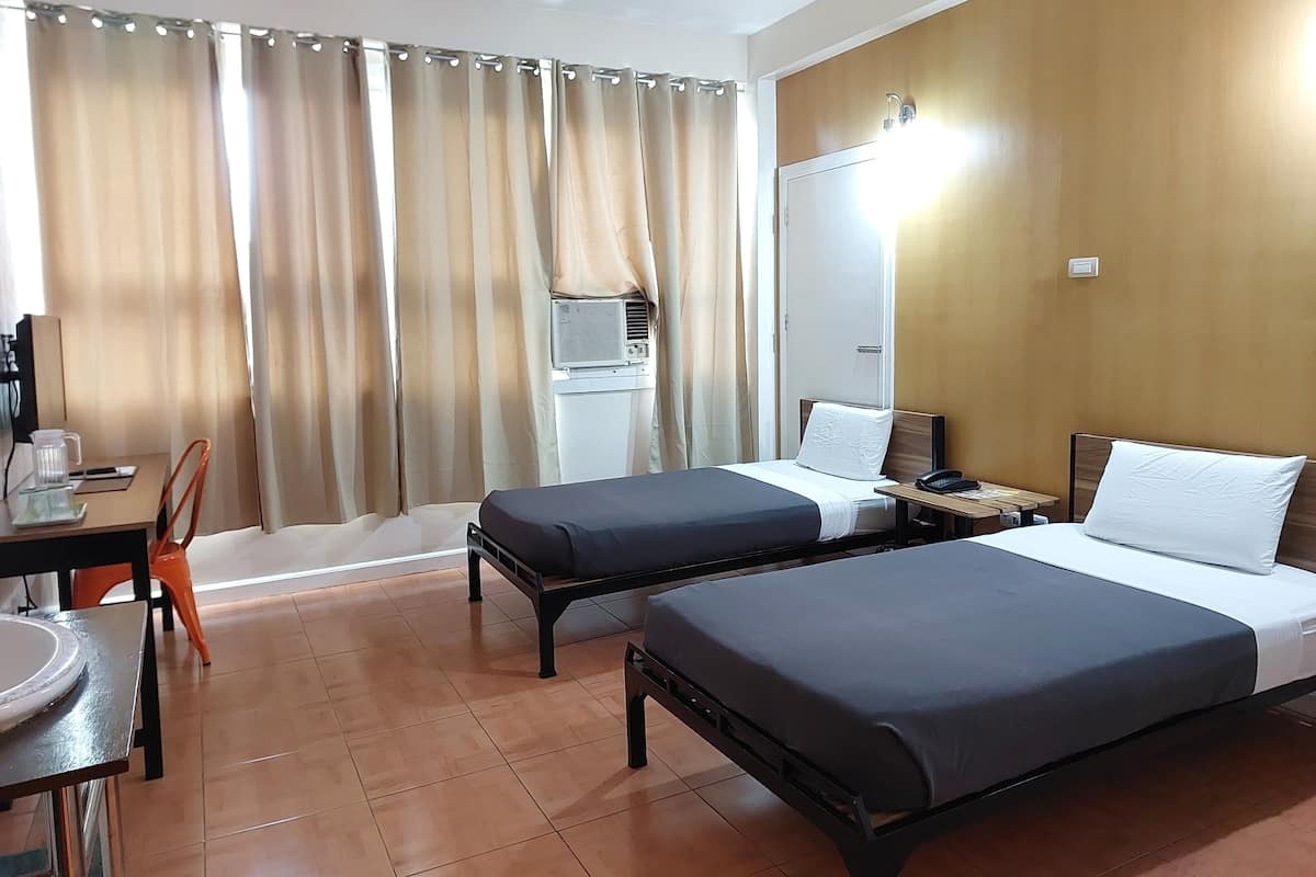 A hotel room with two beds, a desk with a chair, a small table, and a wall-mounted air conditioning unit.