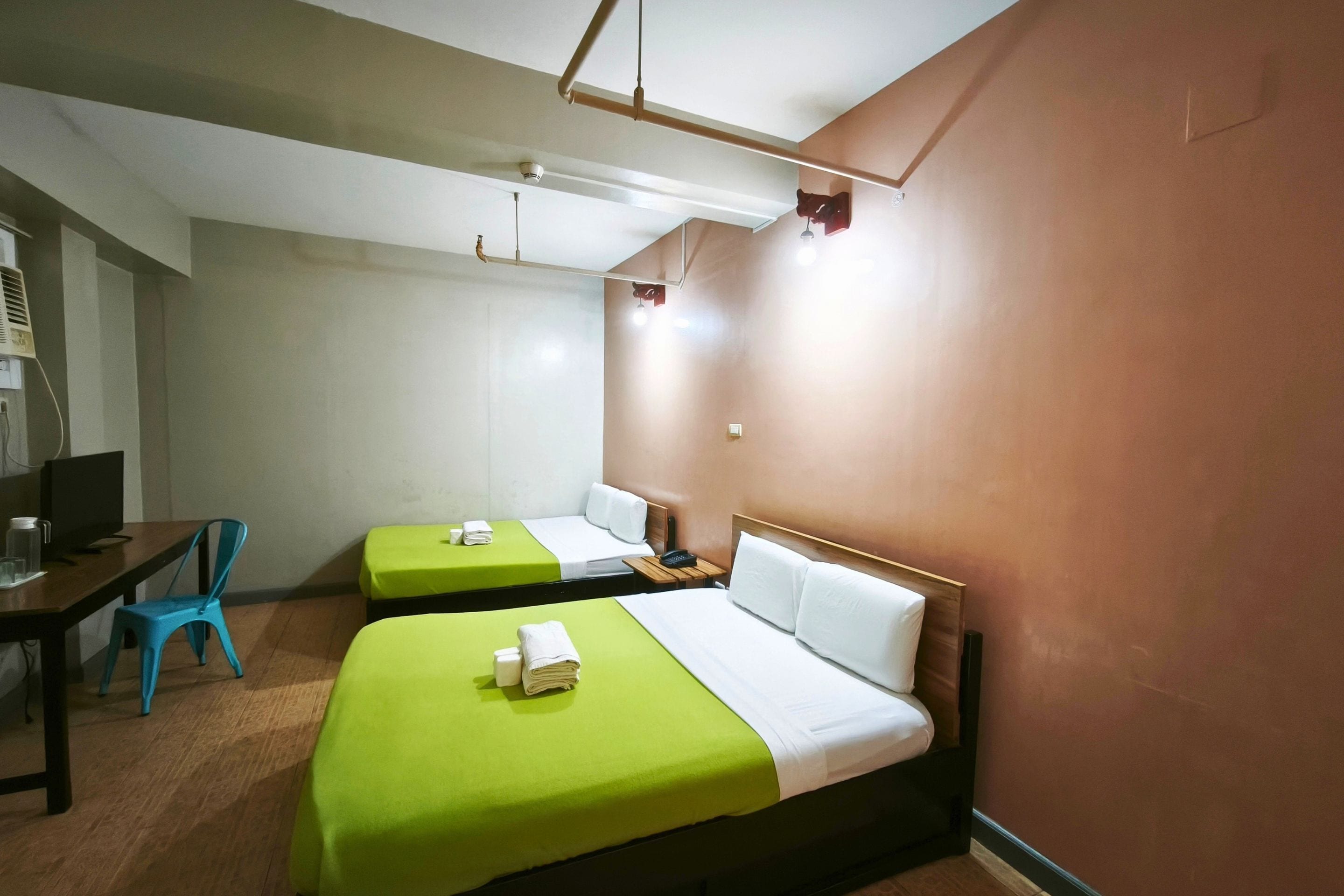 A hotel room with two single beds, a desk with a chair, a television, and a wall-mounted heater.