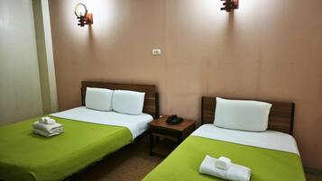 A hotel room with two single beds, green bedspreads, white pillows, a bedside table with a phone, and wall-mounted light fixtures.
