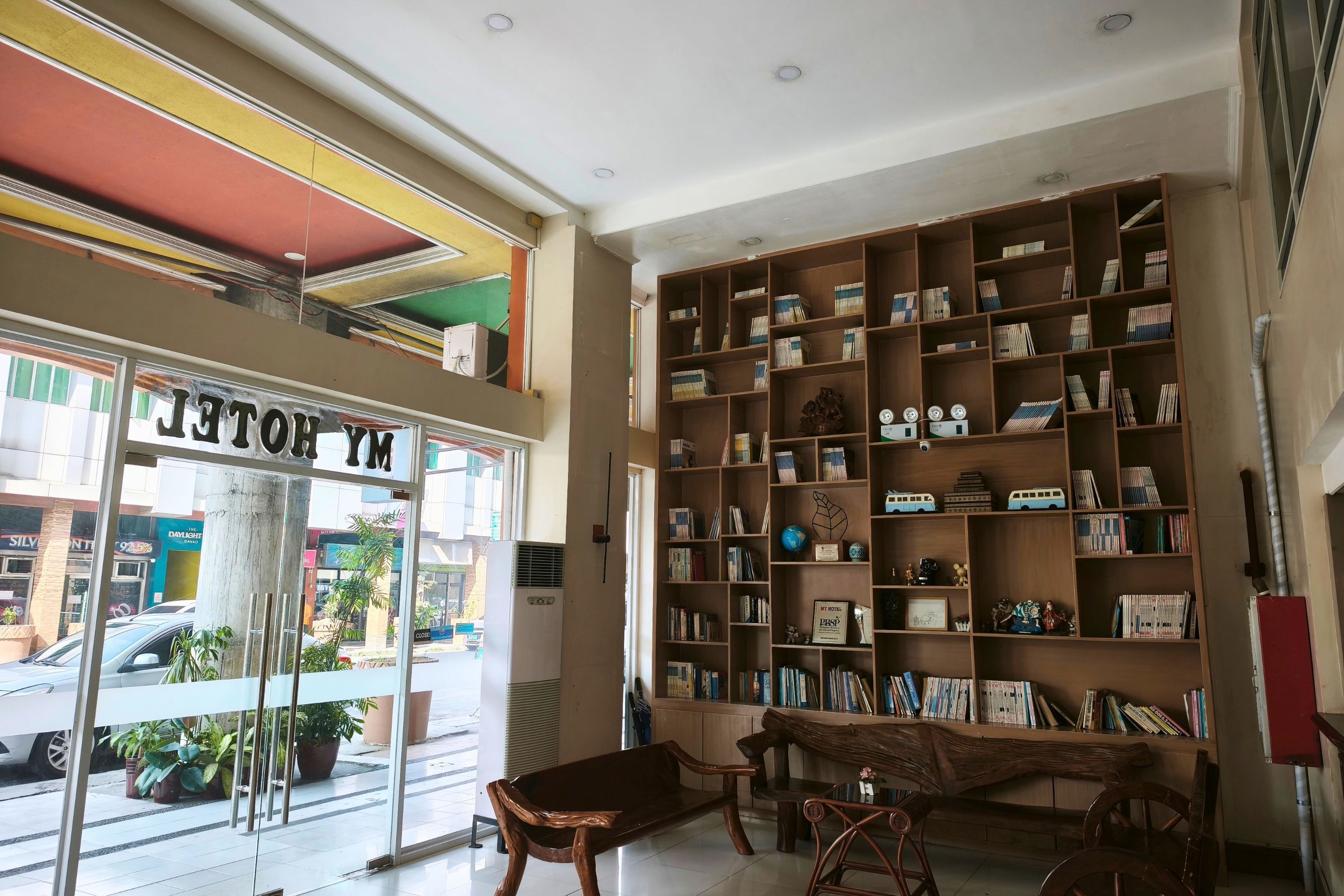 Un hall de hotel con una amplia estantería, un banco y vistas a la calle.