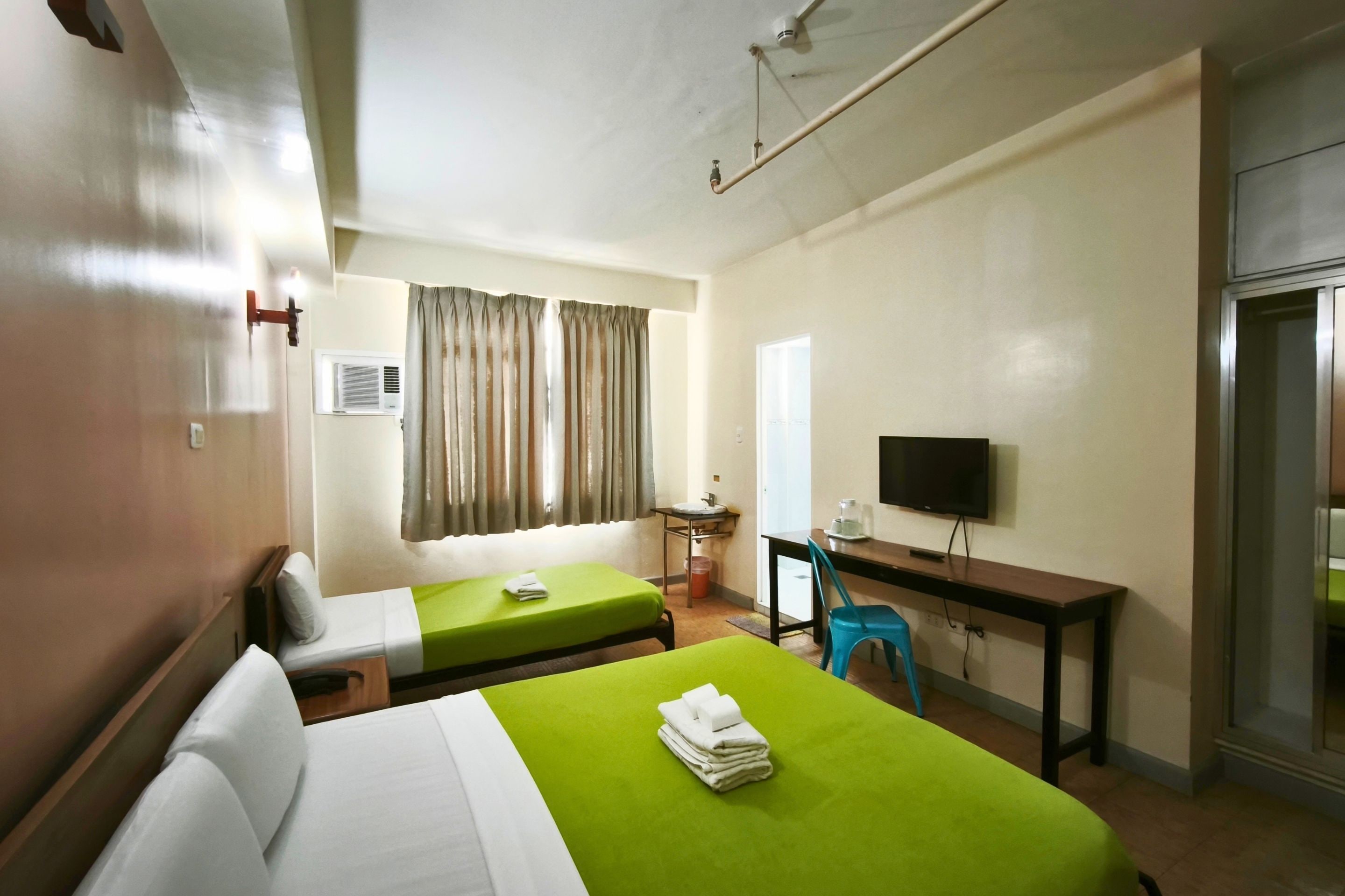 A hotel room with two beds, a desk with a chair, a television, and a window with curtains.