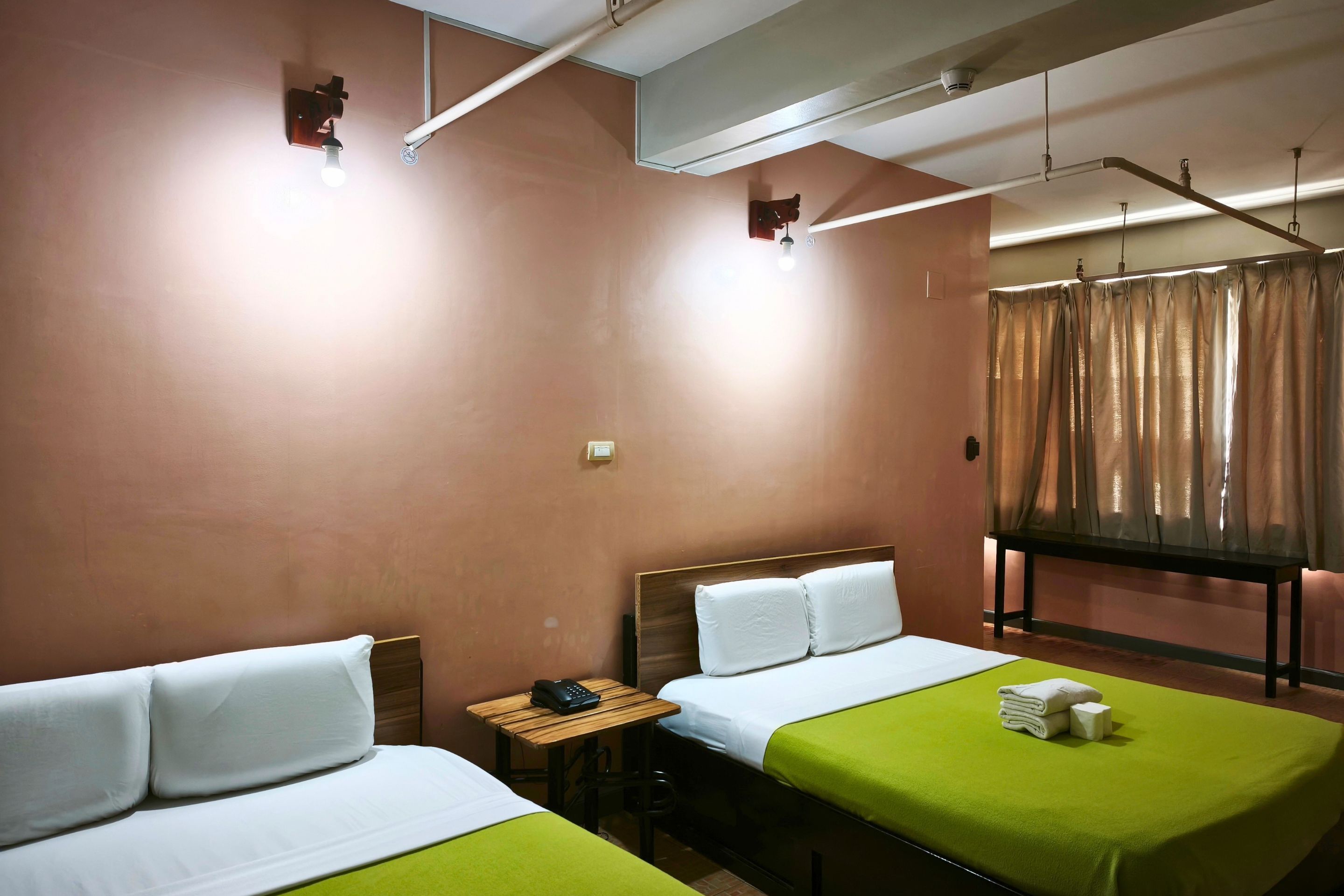 Habitación de hotel con dos camas, una mesita con un teléfono y una ventana con cortinas.