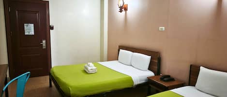 Quarto de hotel com duas camas, uma porta de madeira, uma mesa pequena com telefone e um aplique na parede.