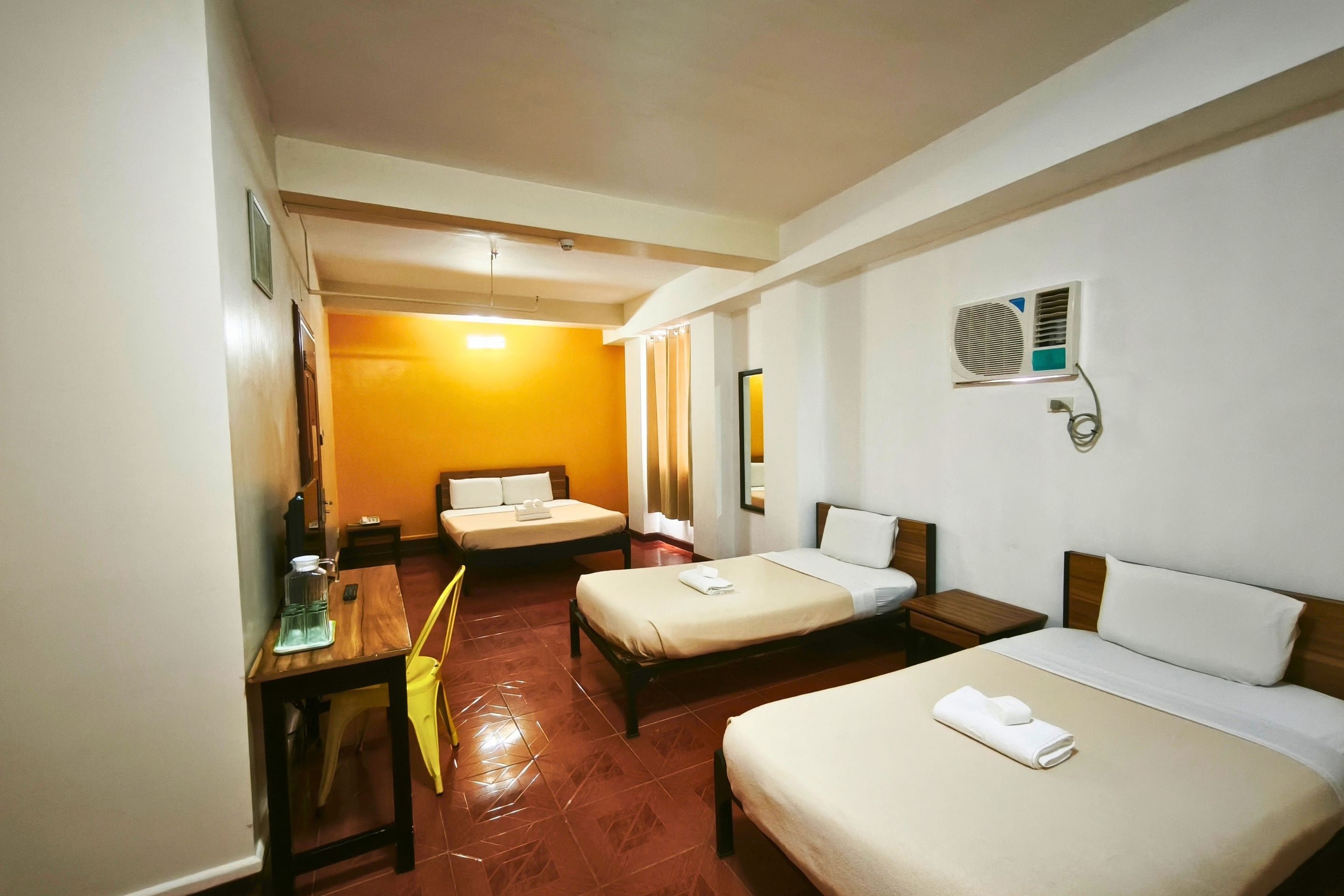 A hotel room with two beds, a desk, a chair, a mirror, and a window.