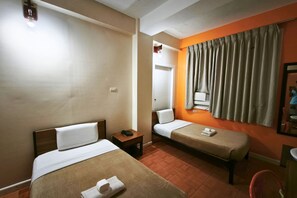Une chambre d’hôtel avec deux lits, une table de chevet avec un téléphone, un miroir et une fenêtre avec des rideaux.