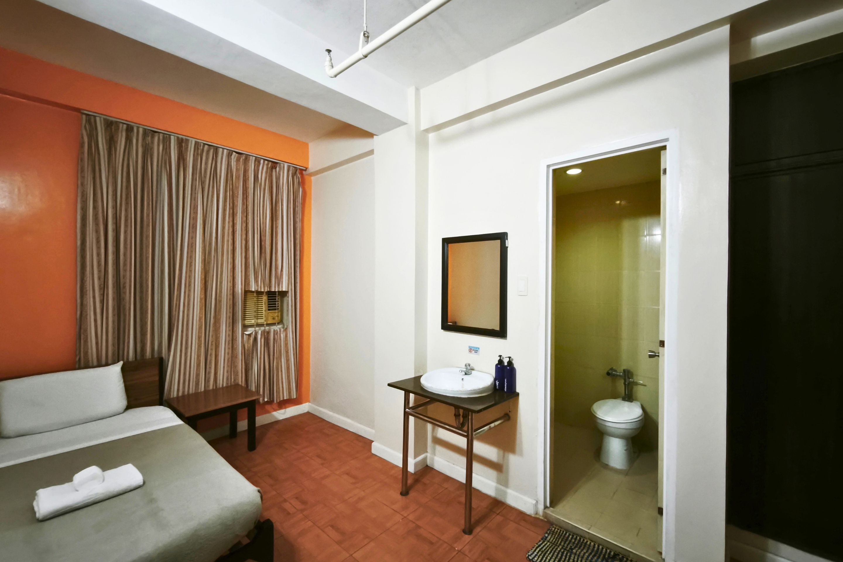 A hotel room with a bed, a small table with a mirror, a sink, and a toilet.
