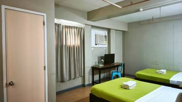 A hotel room with two beds, a desk with a computer, a window with curtains, and a ceiling fan.