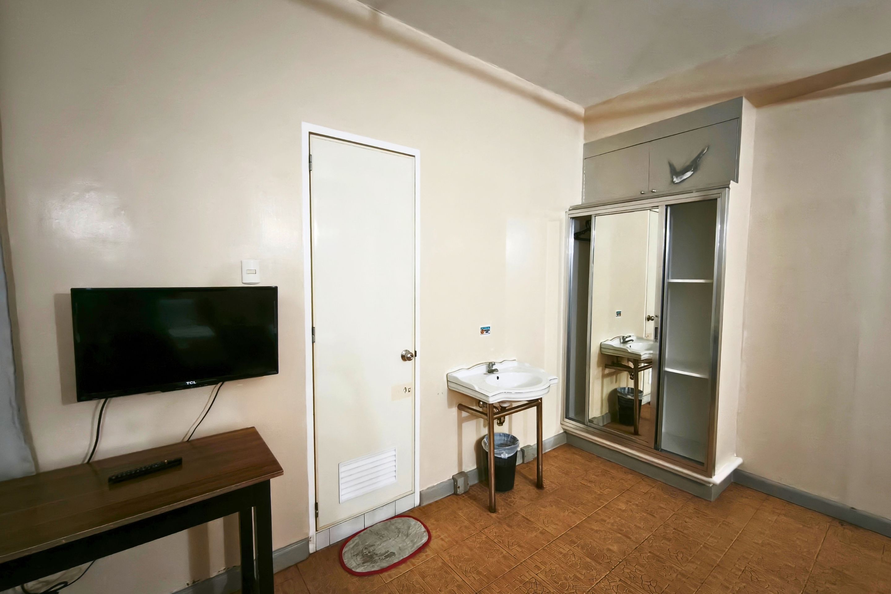 A bathroom with a toilet, sink, and shower. There is a television on a stand and a door with a handle.