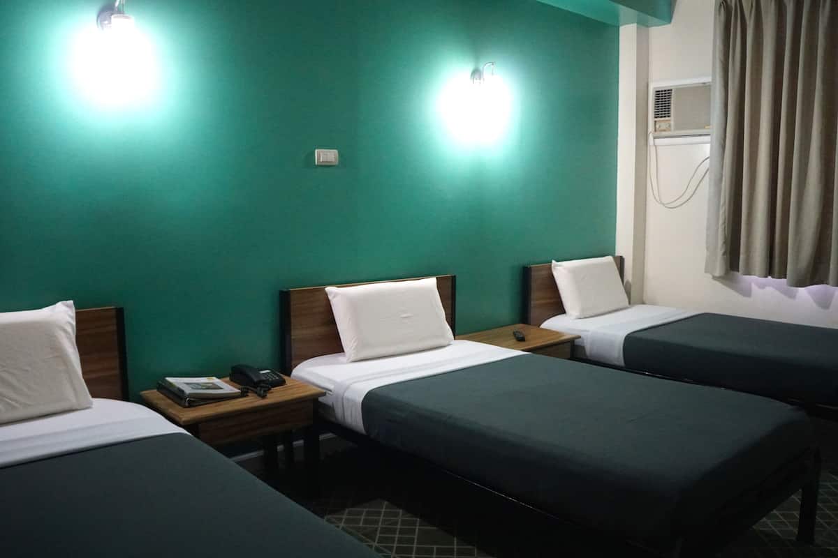 A hotel room with three single beds, a wooden nightstand with a phone and book, and a wall-mounted air conditioning unit.