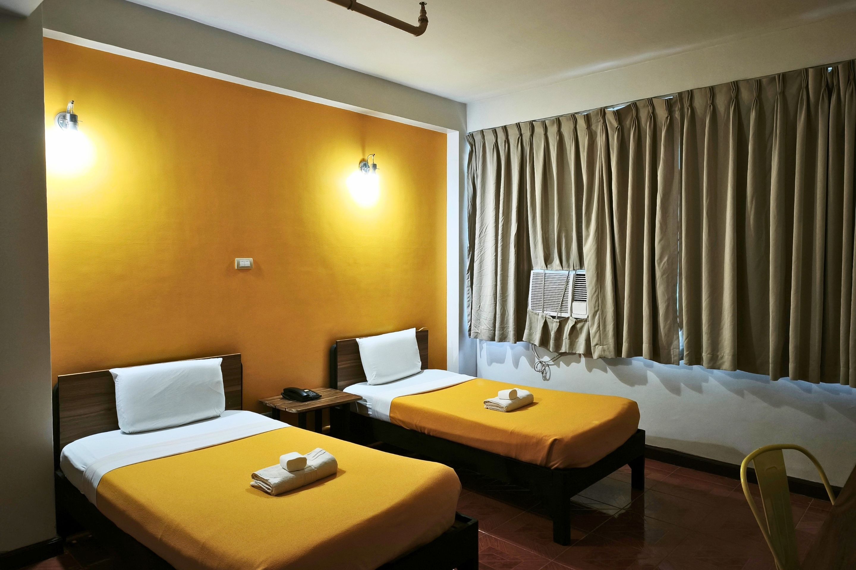A hotel room with two single beds, a bedside table with a phone, and a window with curtains.