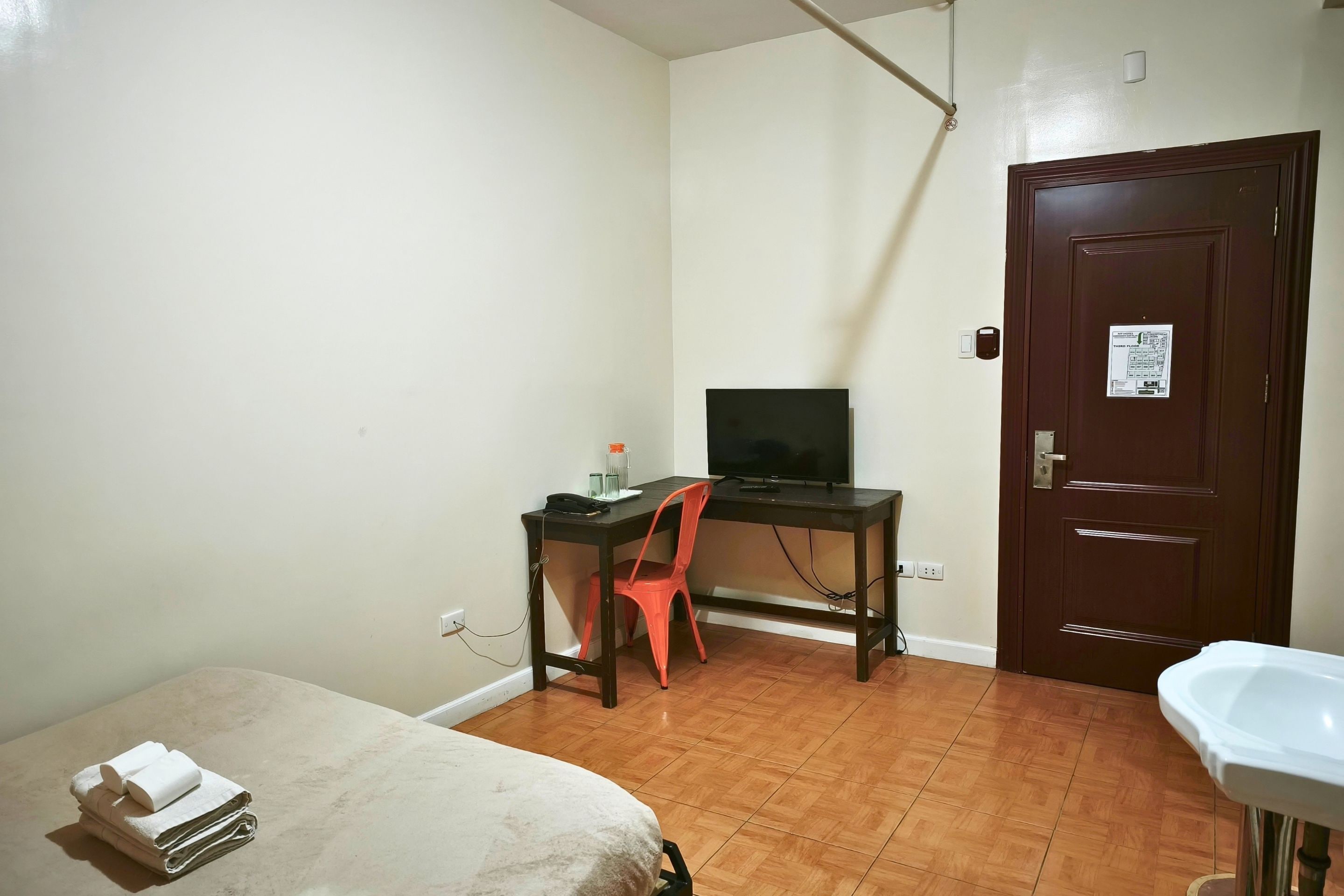 A small room with a bed, a desk with a computer, a door, and a bathroom.
