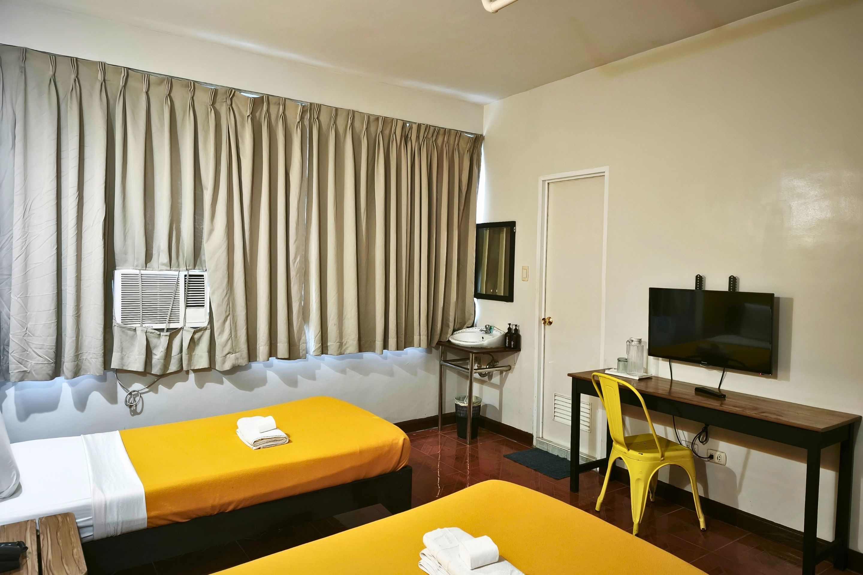 A hotel room with two beds, a desk with a TV, a chair, and a window with curtains.