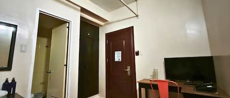 A small room with a desk, chair, television, and a door leading to another room.