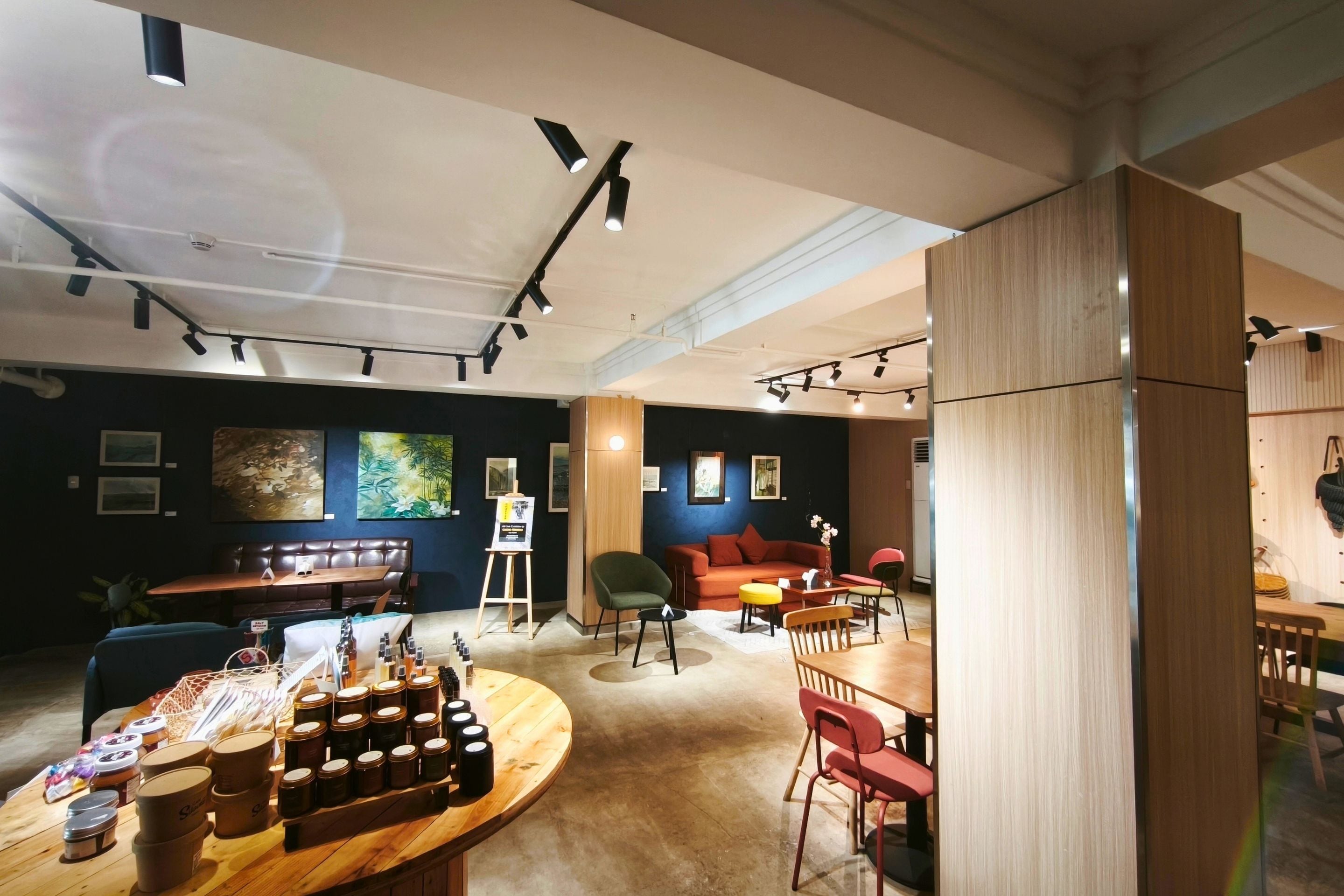 Een modern interieur met een ronde houten tafel waarop potten staan, een zithoek met een bank en stoelen, en kunstwerken aan de muren.