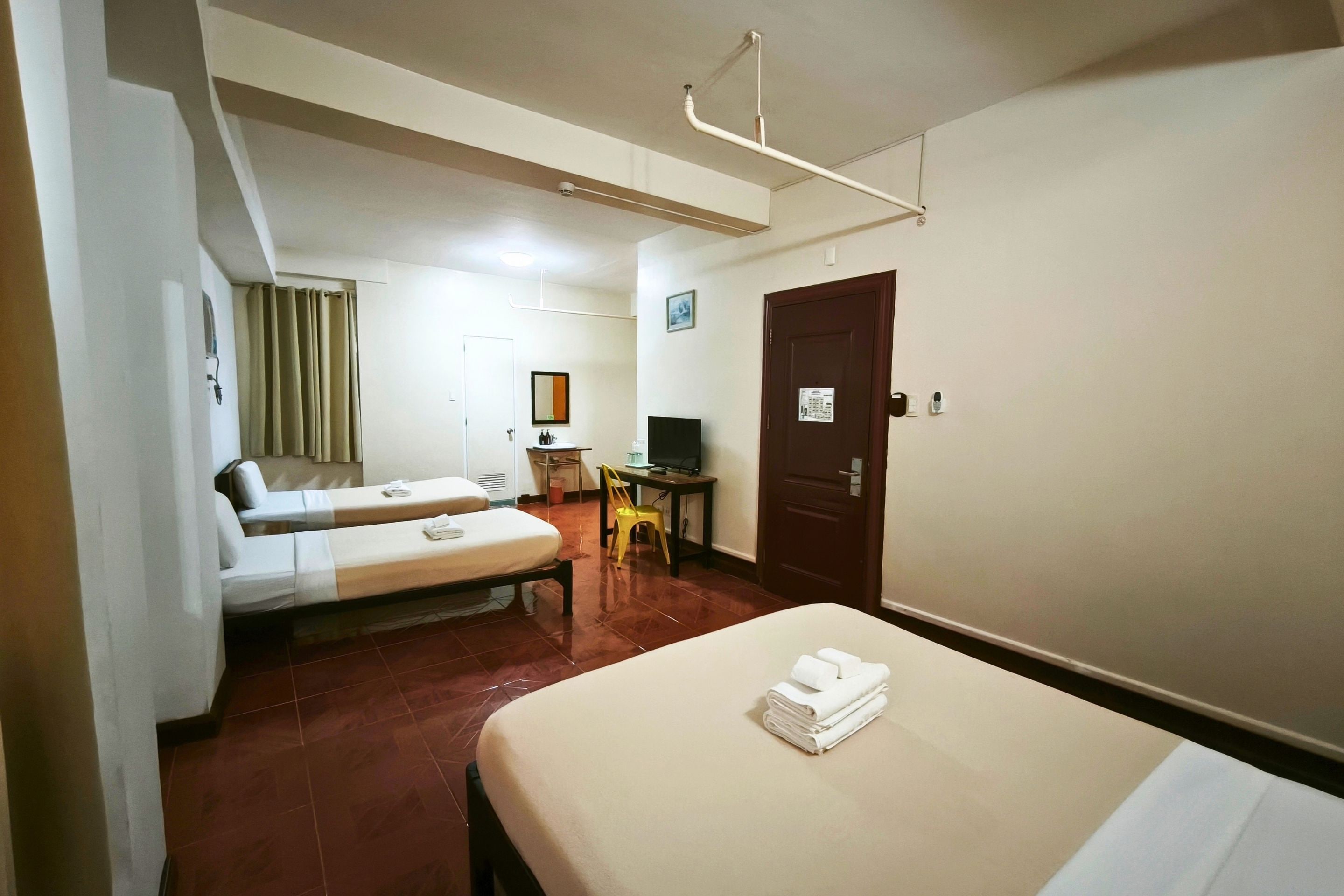 A hotel room with two beds, a desk, a chair, a television, and a door.