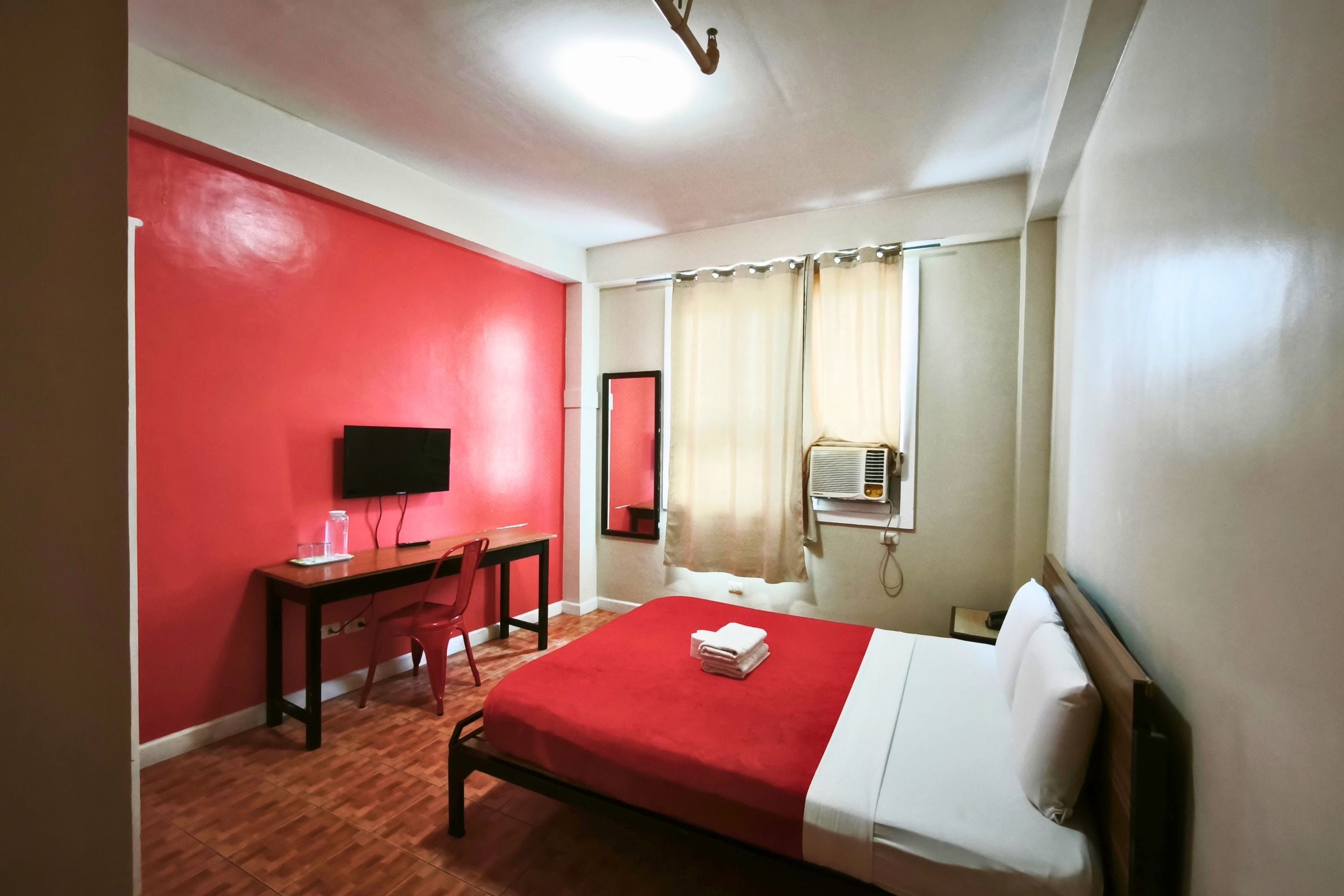 A hotel room with a bed, a desk, a chair, a television, and a window with curtains.