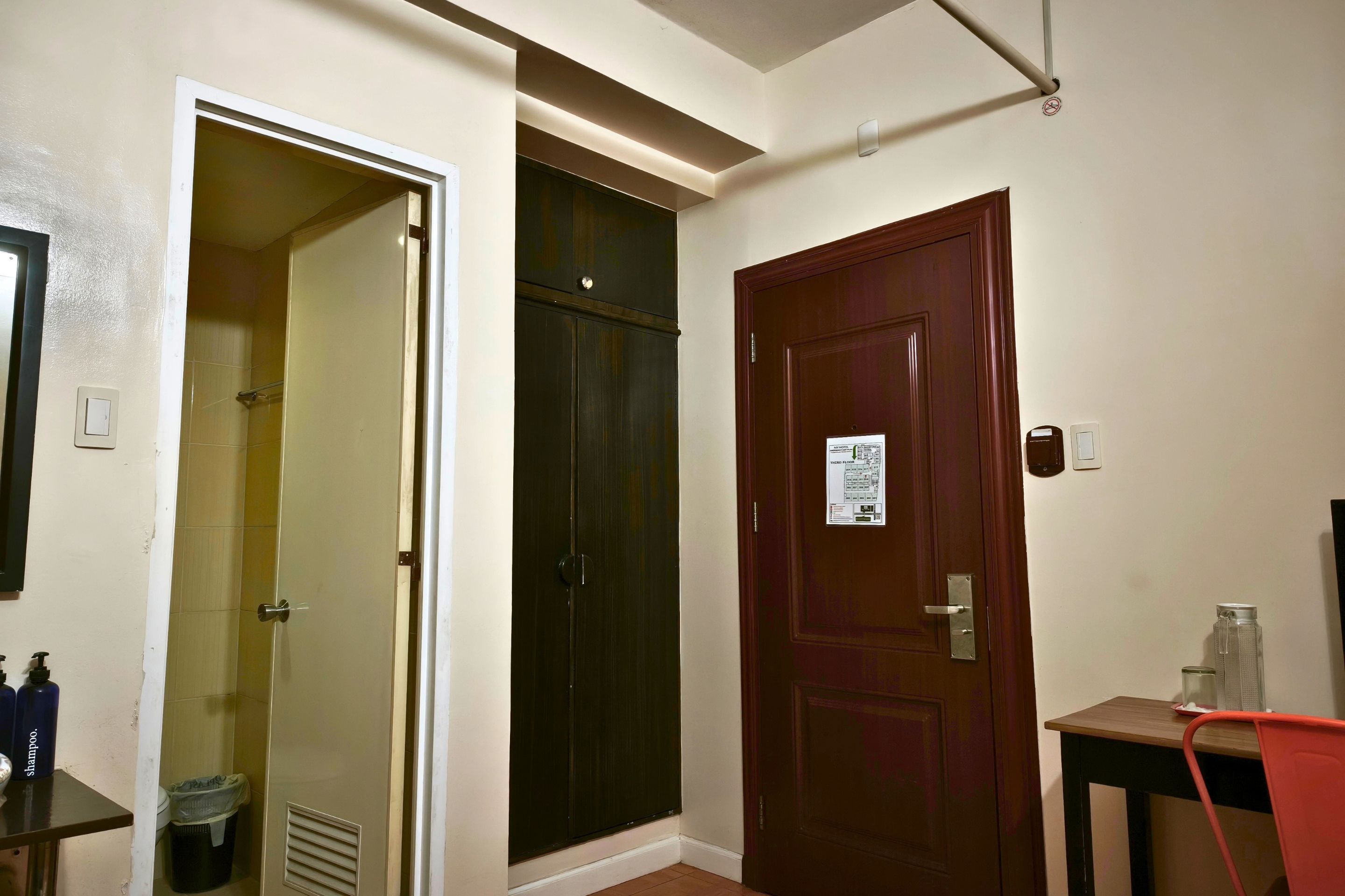 Una camera d'albergo con porta chiusa, bagno con doccia e un piccolo tavolo con una sedia.
