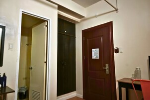 Habitación de hotel con puerta cerrada, baño con ducha y una pequeña mesa con una silla.