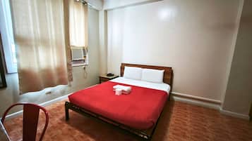 A hotel room with a bed, a chair, a bedside table with a phone, and a window with curtains.