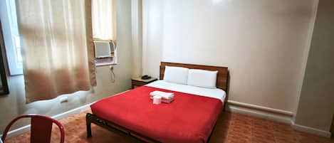 Habitación de hotel con una cama, una silla, una mesita de noche con teléfono y una ventana con cortinas.