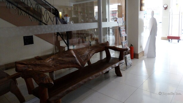 A wooden bench in a lobby with a staircase and a glass wall. - My Hotel (Davao)