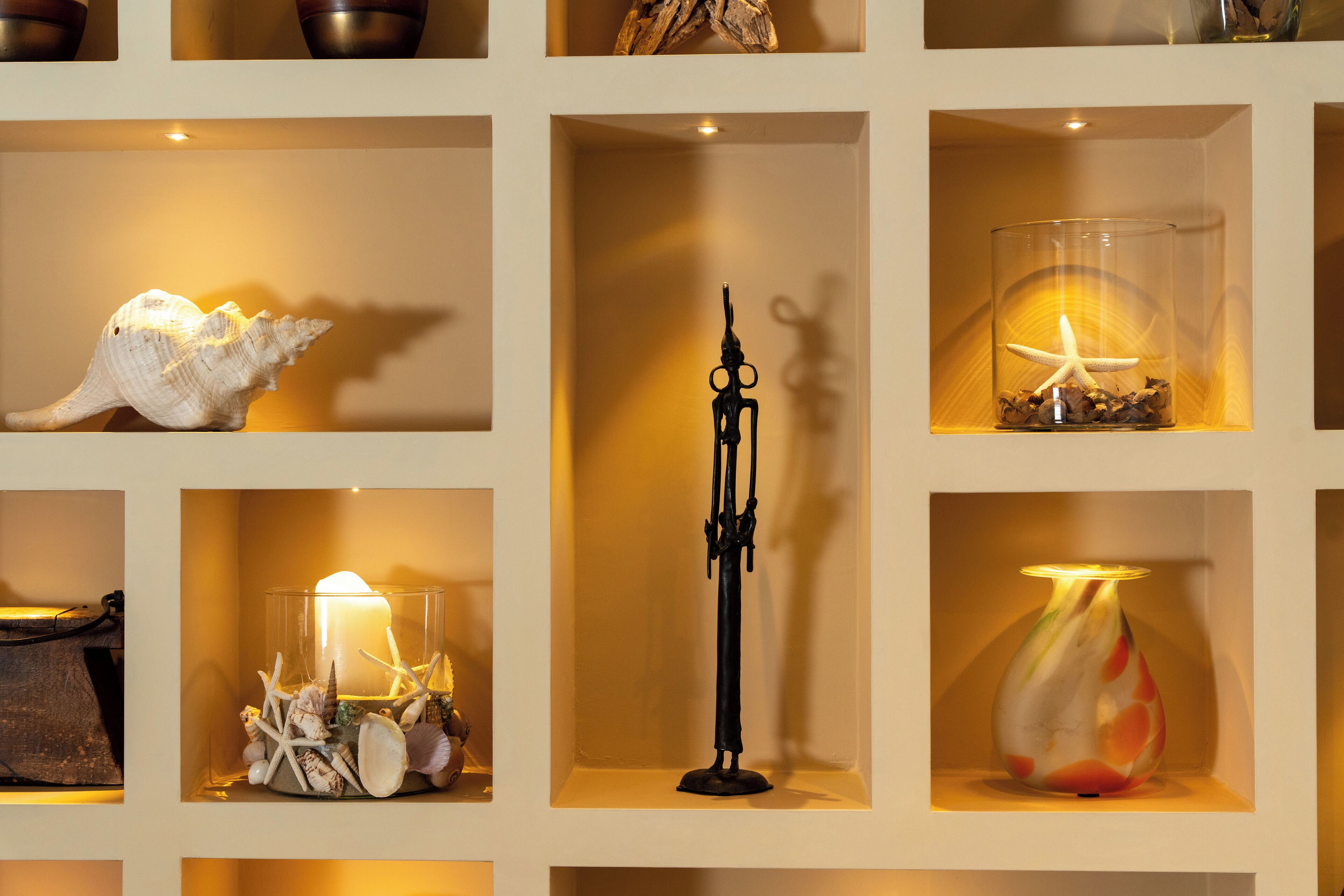 Uma parede com várias prateleiras exibindo objetos decorativos, incluindo conchas, uma vela e um vaso de vidro com uma estrela-do-mar.