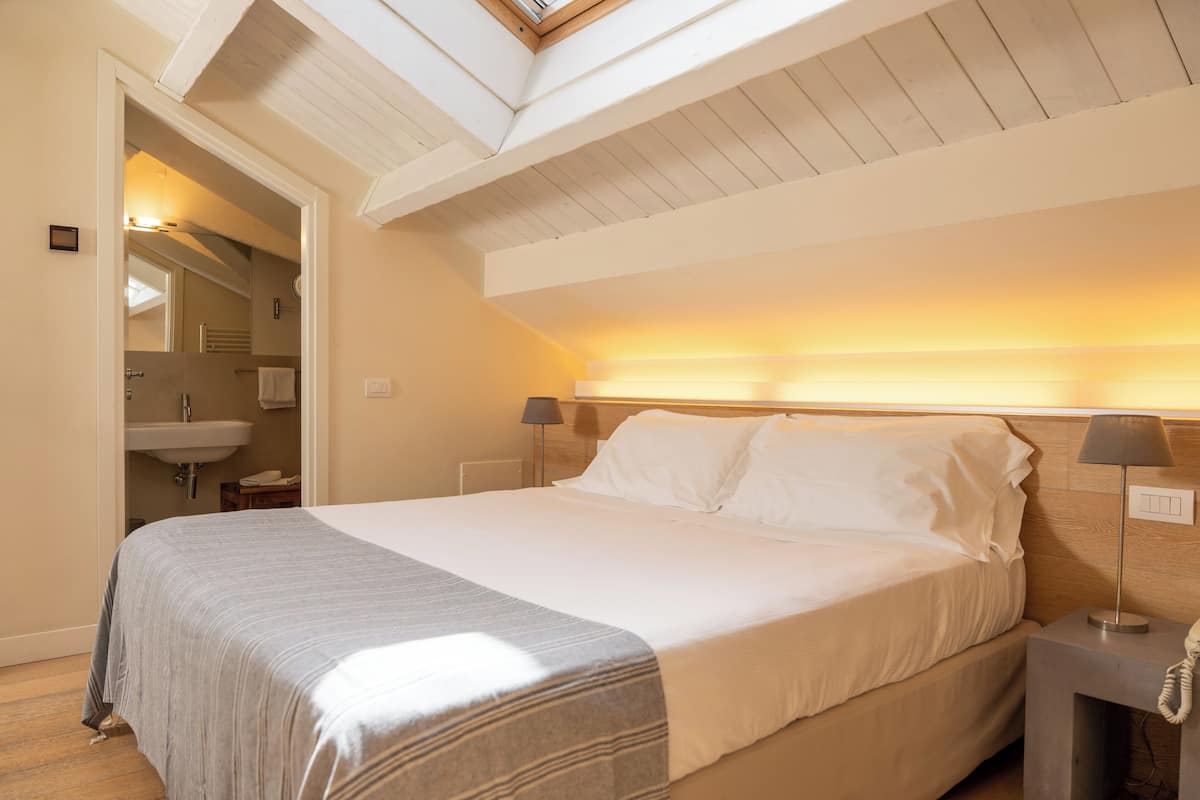 A bedroom with a large bed, bedside lamps, a nightstand with a phone, a wooden headboard, and a skylight above.
