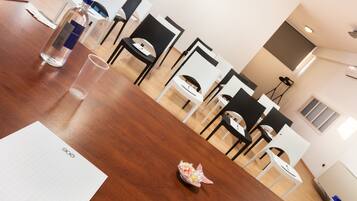 Une salle de conférence avec une table en bois, des chaises, une bouteille, un verre et un arrangement floral.