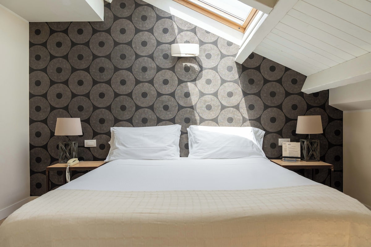 A hotel room with a large bed, two bedside tables, lamps, a telephone, and a patterned wallpaper.