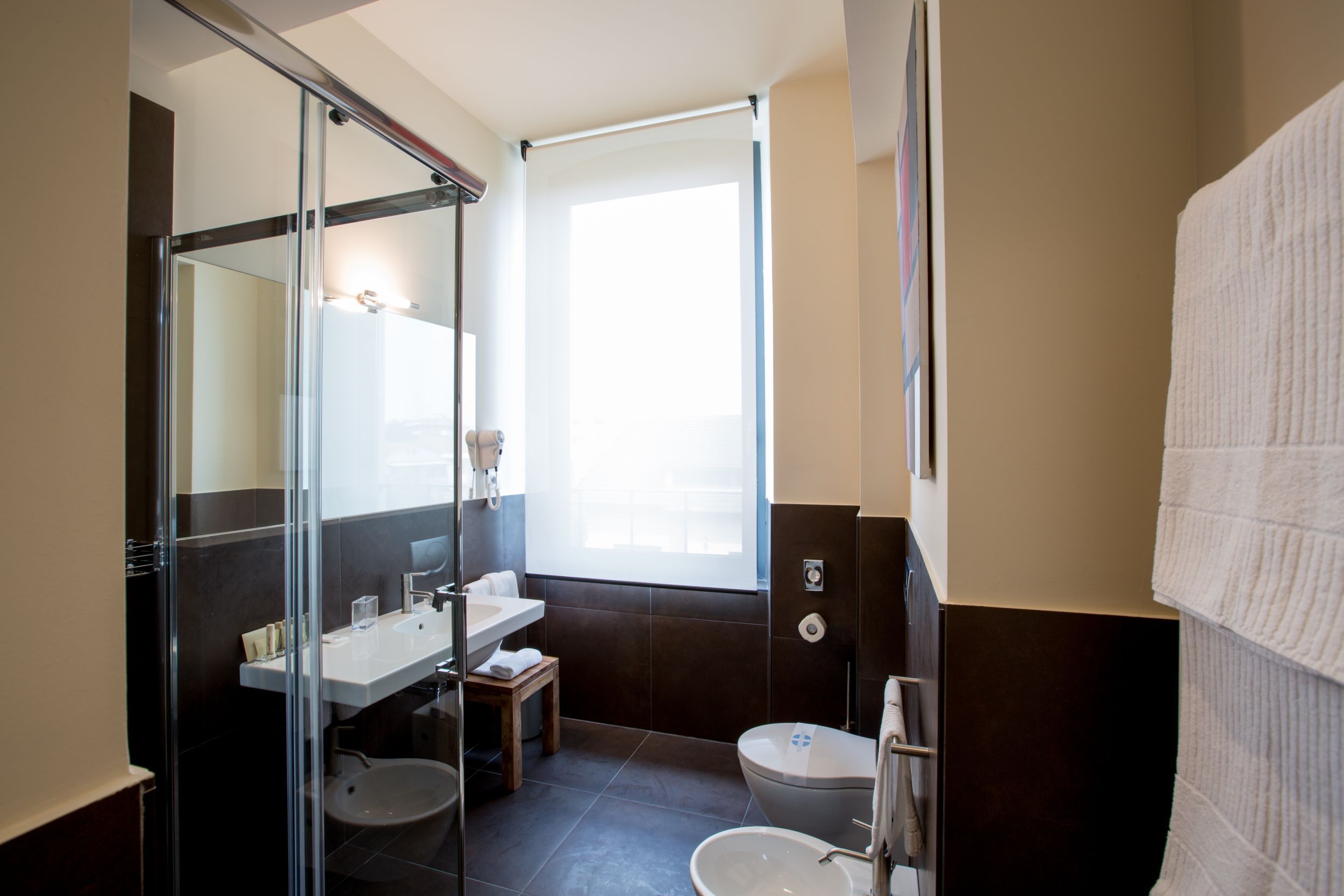 A modern bathroom with a glass shower enclosure, a sink, a toilet, and a large window providing natural light.