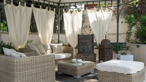 A covered outdoor seating area with wicker furniture, a Buddha statue, and a birdcage. - Hotel 900 (Giulianova)