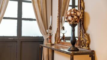 Une pièce au style rétro, dotée d’un grand miroir, d’un vase décoratif contenant des coquillages et d’une fenêtre agrémentée de rideaux.
