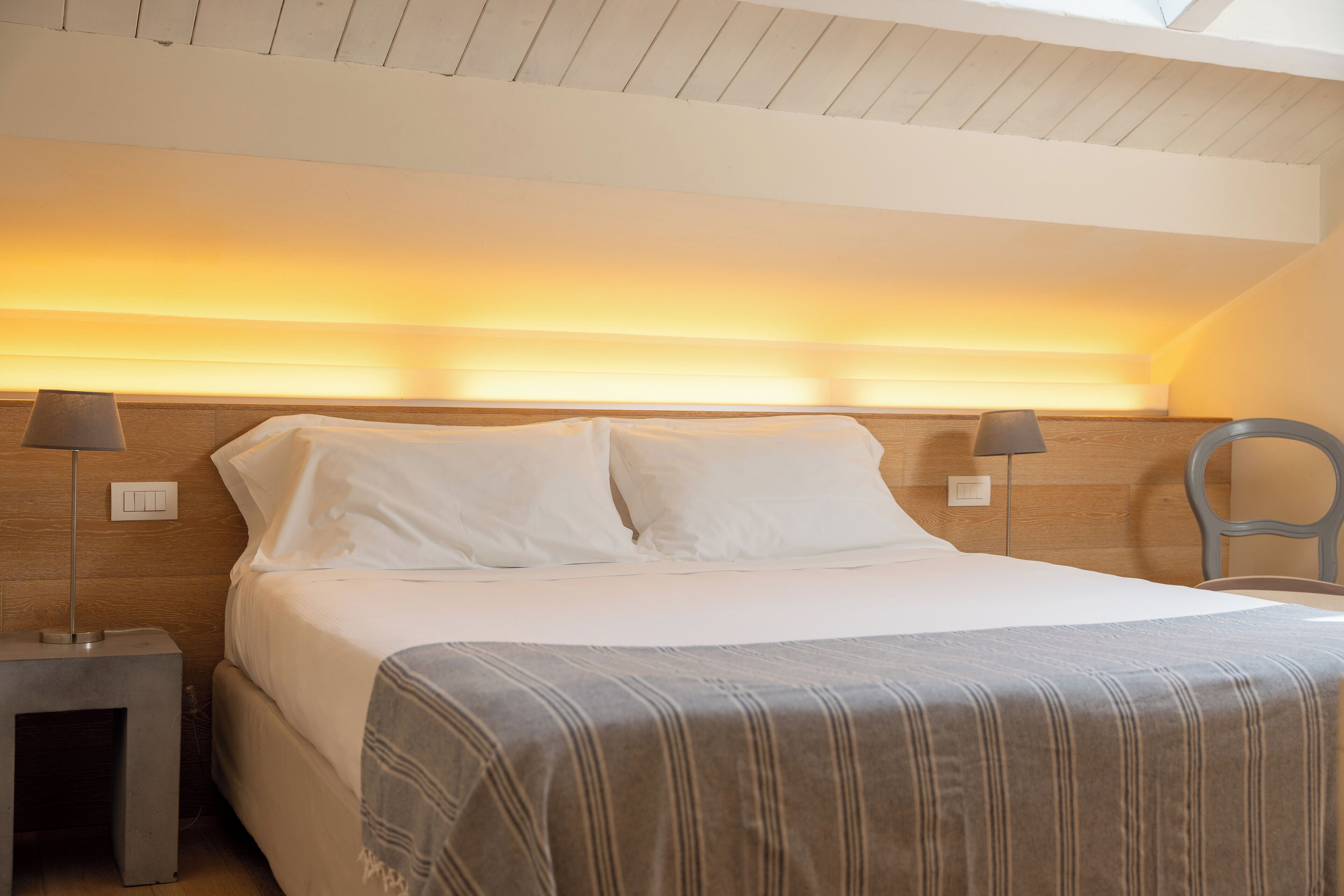 A neatly made bed with white linens and a striped blanket, two bedside lamps, and a wooden headboard.